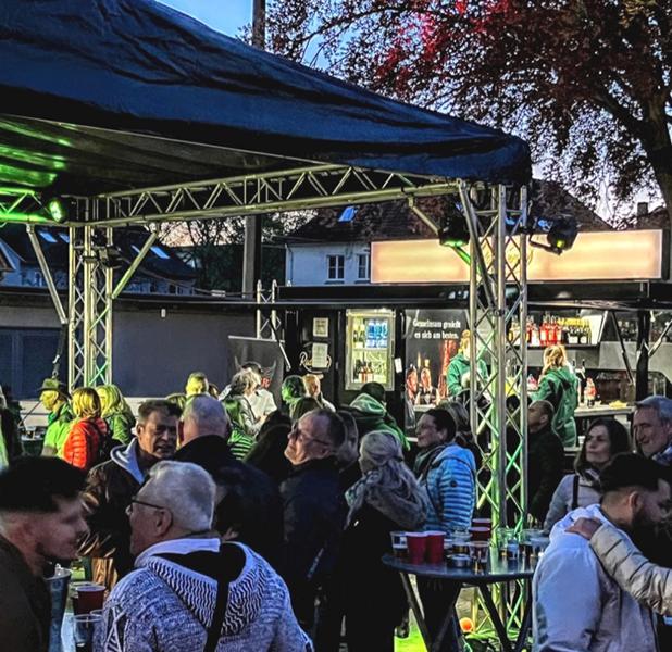 Menschen stehen vor einer Freilichtbühne im Dämmerlicht.